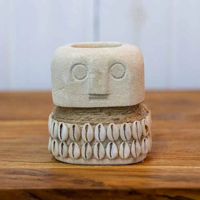 Porta-vela tribal com adorno de búzios naturais e corda de fibra sobre mesa de madeira.