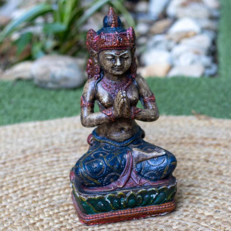 Estátua de mulher balinesa em posição de meditação sentada, esculpida em cimento com detalhes coloridos.