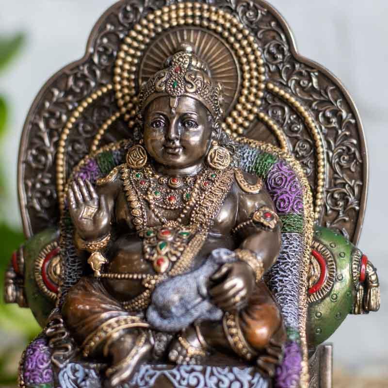 Detalhe do rosto sereno de Kubera entronizado, destacando os ornamentos dourados e a coroa trabalhada da divindade hindu.