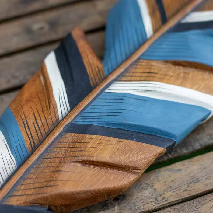 Detalhe de pena esculpida em madeira com pintura em tons de azul, branco e marrom.