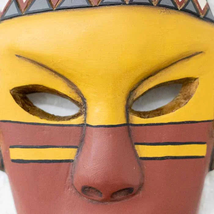 Escultura facial indígena com grafismos em preto e amarelo representando rituais ancestrais.