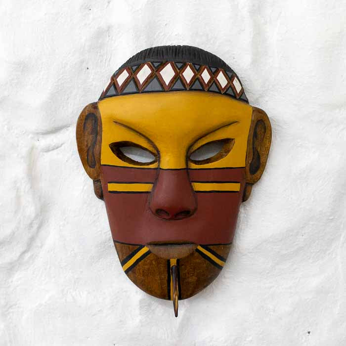 Máscara indígena artesanal entalhada em madeira com pintura tradicional Pataxó em amarelo e vermelho.