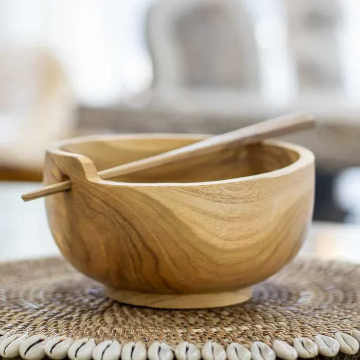 Bowl artesanal esculpido à mão em madeira teca com hashis encaixados na borda, peça funcional e decorativa que representa o artesanato balinês.