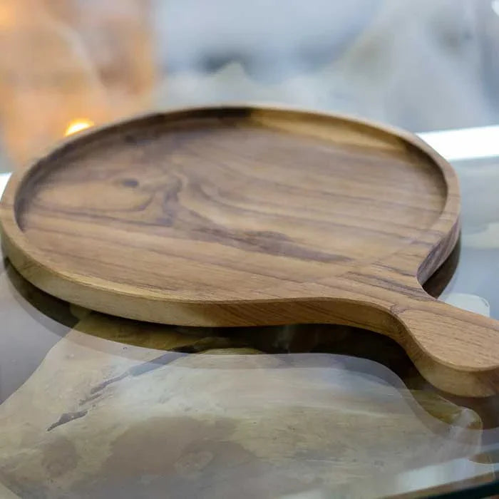Tábua artesanal redonda em madeira teca com bordas suaves e textura natural, perfeita para servir pizzas e realçar a estética rústica da mesa.