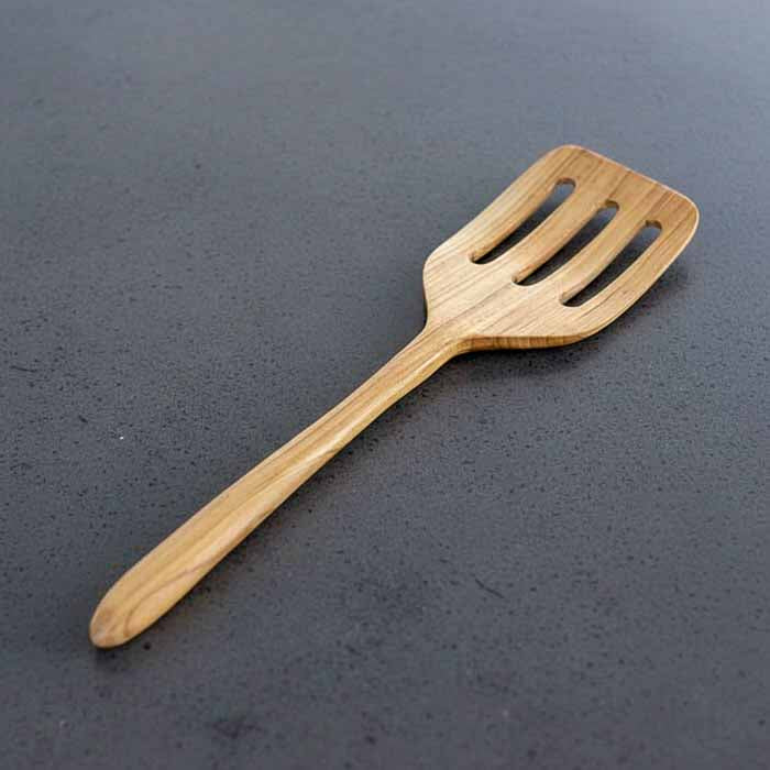 Espátula vazada artesanal em madeira teca produzida em Bali com acabamento fosco polido e cabo anatômico ideal para cozinhar e servir alimentos.