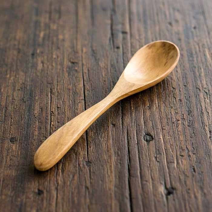 Colher de pau em teca originária de Bali com cabo anatômico e textura natural usada para preparar alimentos com leveza e segurança.