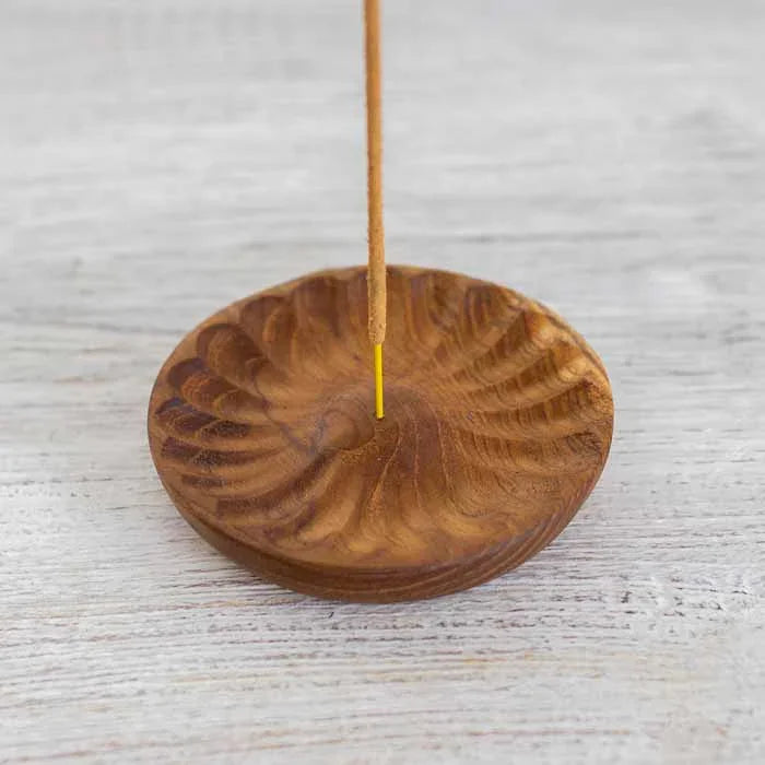 Incensário artesanal em madeira teca com design circular e entalhes em espiral.