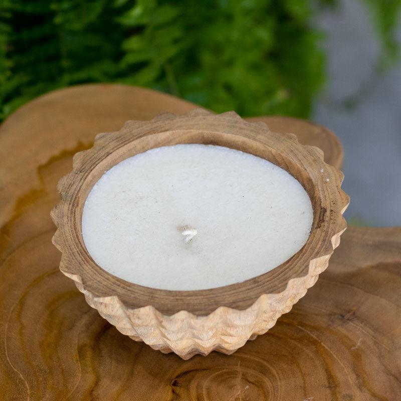 Vela artesanal em bowl de madeira rústica esculpida à mão em Bali, destacando os veios naturais da madeira.
