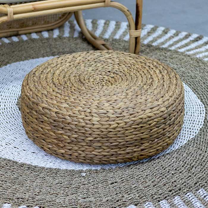 Puff em rattan natural com formato redondo e estrutura interna usado para sentar ou apoiar os pés em composições boho.