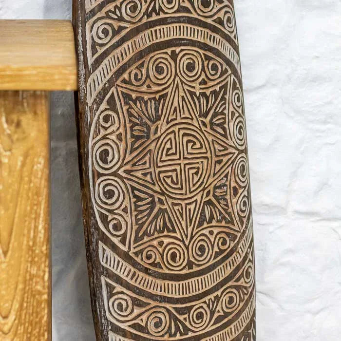 Prancha artesanal de Timor com gravuras tribais detalhadas e tons terrosos, representando a tradição cultural e o valor simbólico do artesanato asiático. 