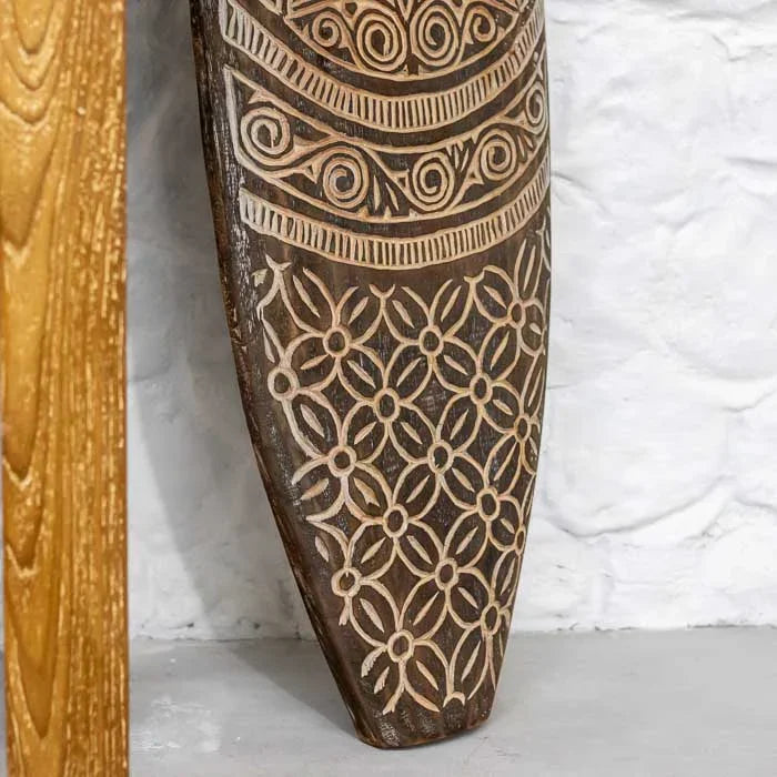 Detalhe da prancha entalhada timorense em madeira natural, com padrões geométricos e espirais, peça de decoração artesanal e espiritual única. 