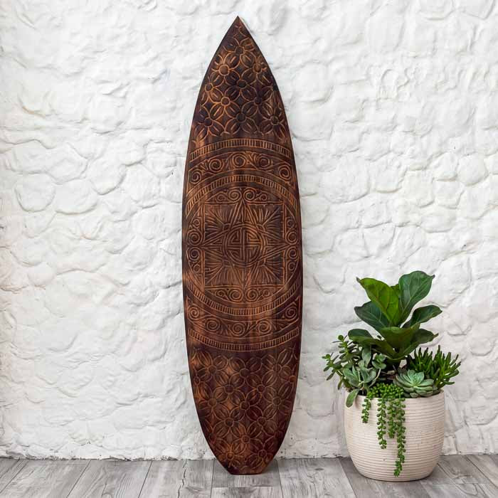 Prancha étnica em madeira entalhada manualmente por artesãos de Timor, com desenhos tribais em espiral e formas geométricas que simbolizam harmonia e ancestralidade. 