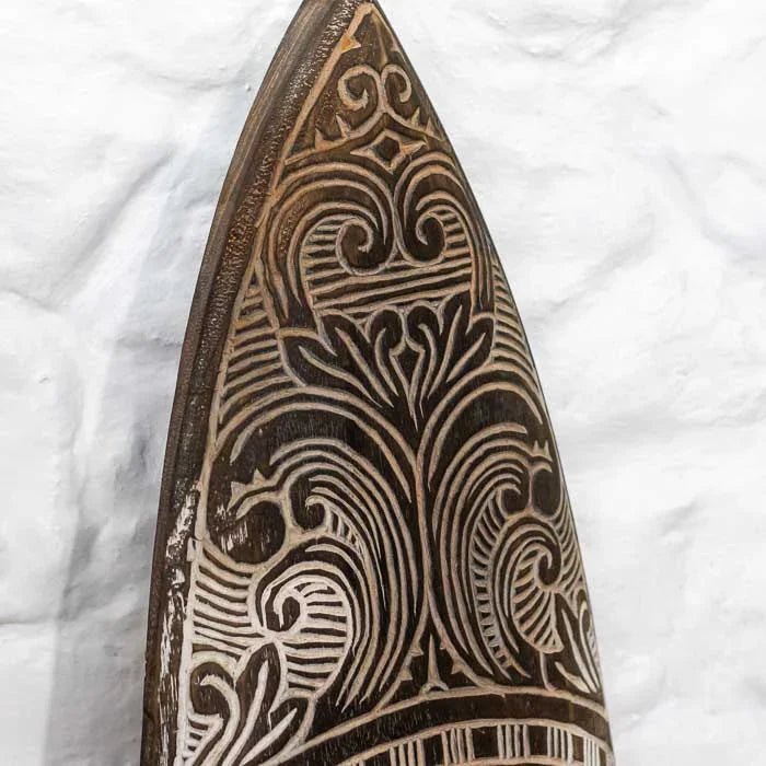 Prancha artesanal de Timor com gravuras tribais detalhadas e tons terrosos, representando a tradição cultural e o valor simbólico do artesanato asiático. 