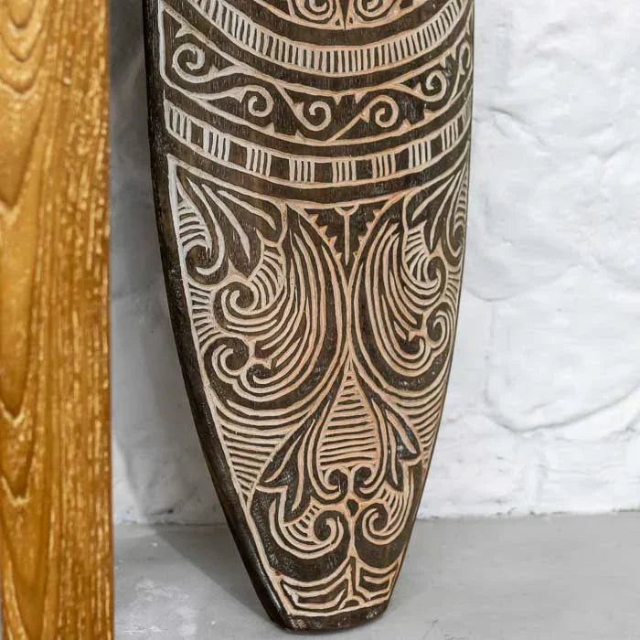 Detalhe da prancha entalhada timorense em madeira natural, com padrões geométricos e espirais, peça de decoração artesanal e espiritual única. 