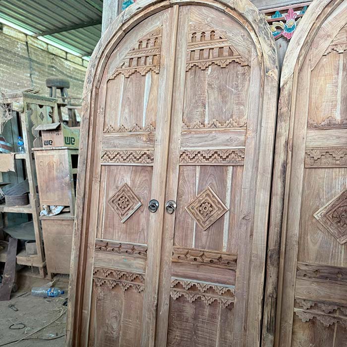 Detalhe dos entalhes superiores em relevo de porta indonésia, destacando a textura da madeira natural.