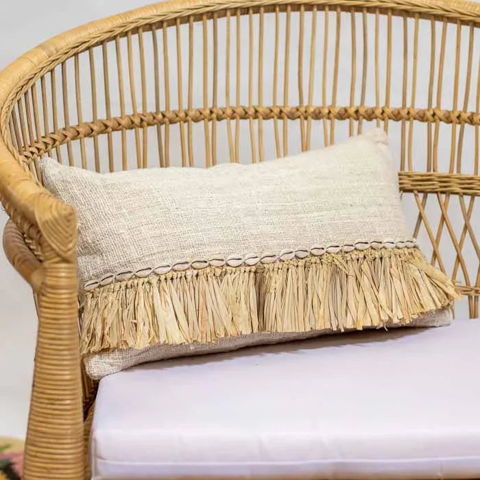 Almofada retangular artesanal com franja de fibra natural e aplicação de búzios. 