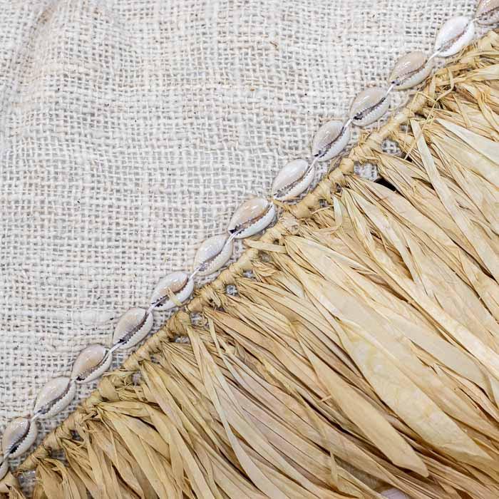 Detalhe da aplicação de búzios (conchas cowrie) e franja na almofada decorativa. 