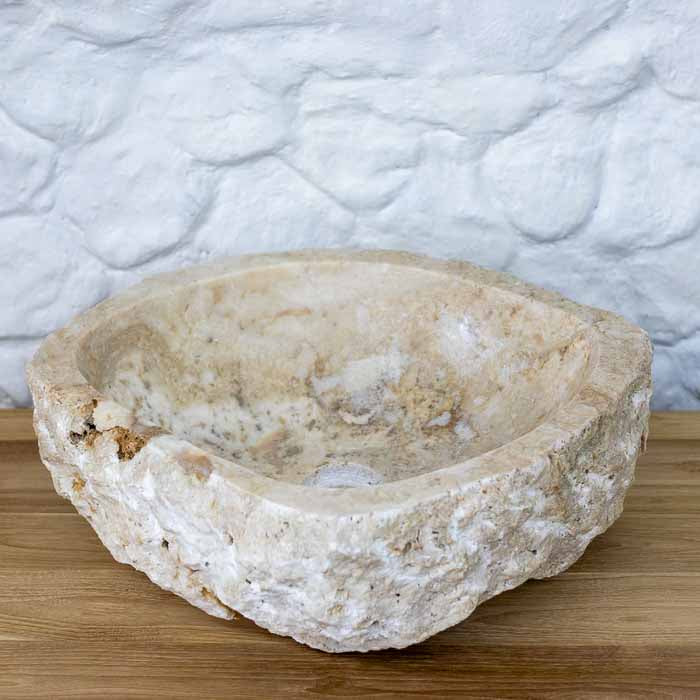 Pia de banheiro em pedra ônix natural balinesa com bordas rústicas e veios orgânicos em tom bege e creme. 