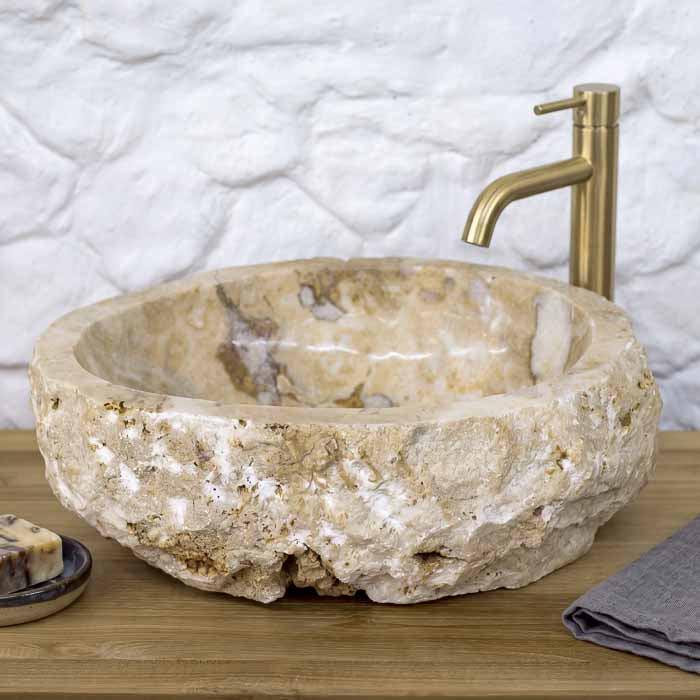 Pia artesanal de bancada em pedra ônix com textura mineral e bordas esculpidas em relevo rústico. 