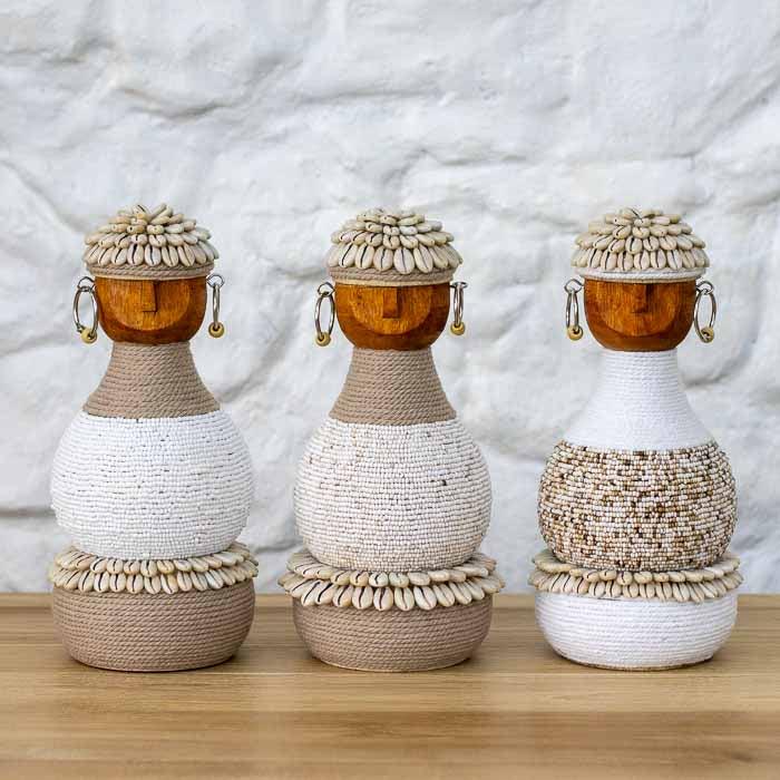 Boneca decorativa de Bali com base adornada por búzios e traços tribais minimalistas.