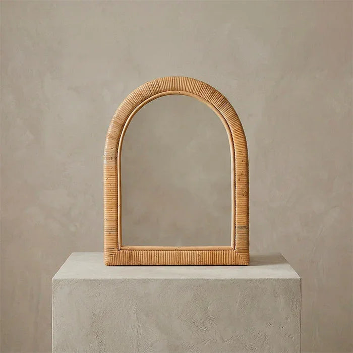 Espelho de parede em formato de arco com moldura detalhada em tramas horizontais de rattan natural.