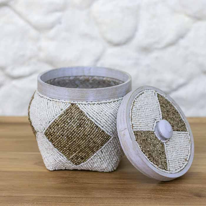 Pote organizador artesanal boho com tampa revestido em miçangas brancas e douradas de Bali sobre mesa de madeira.