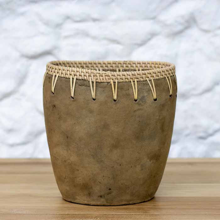 Vaso decorativo artesanal em terracota com borda trançada em rattan natural de Bali sobre mesa de madeira.