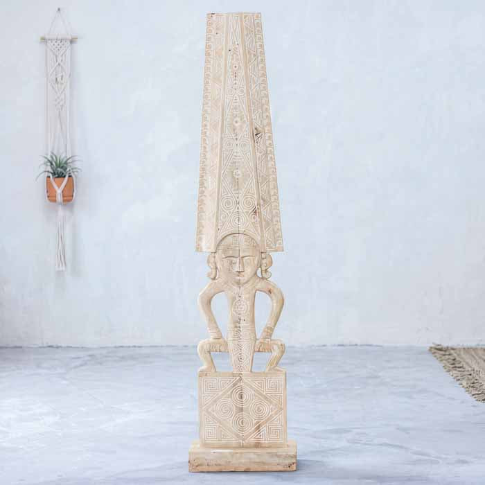 Totem étnico primitivo artesanal com acabamento em pátina clara entalhado em madeira de Timor em hall de entrada.