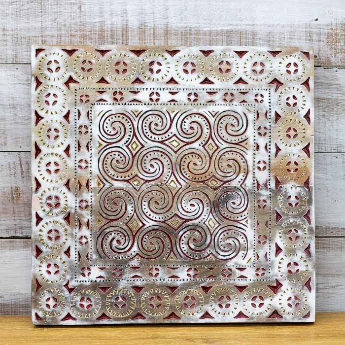 Painel quadrado de 60cm em madeira clara com entalhes espirais complexos e grafismos étnicos de Tana Toraja.