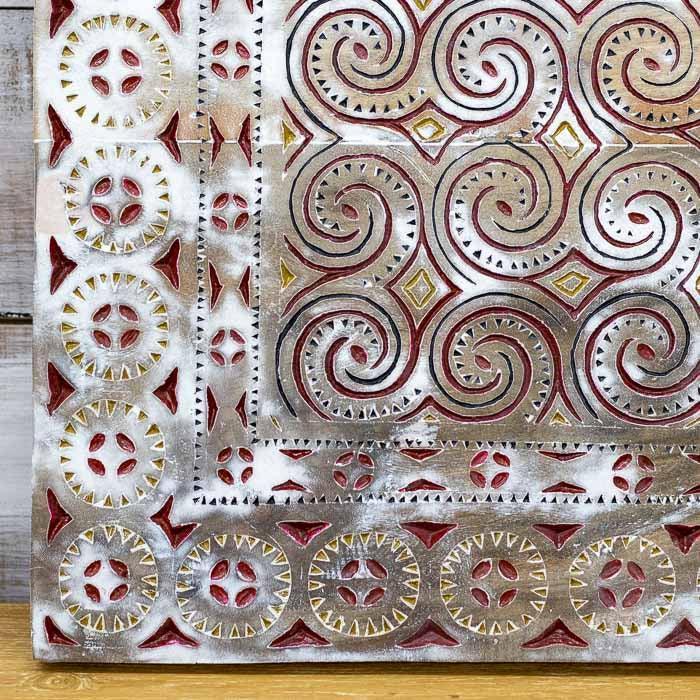Painel decorativo de Tana Toraja evidenciando a profundidade dos entalhes manuais e a pátina branca e vermelha.