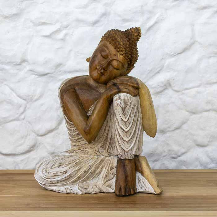 Escultura feita à mão de Buddha relaxando em madeira Teca maciça com manto em pátina branca de Bali sobre mesa.