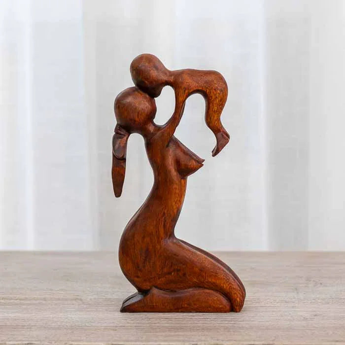 Escultura abstrata em madeira natural representando uma mãe segurando seu filho no alto. 