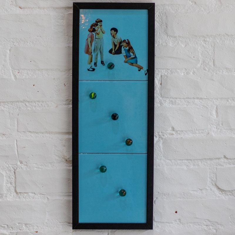 Painel decorativo em azulejos azuis com colagem de crianças brincando com bolas de gude em relevo. 