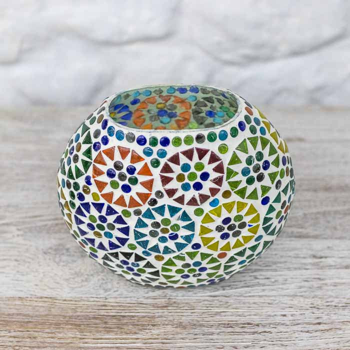 Luminária de mesa esférica em mosaico de vidro colorido acesa sobre superfície rústica.