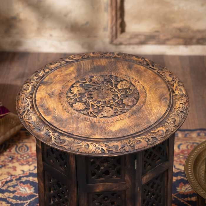 Detalhe dos entalhes florais minuciosos no tampo circular da mesa de apoio.
