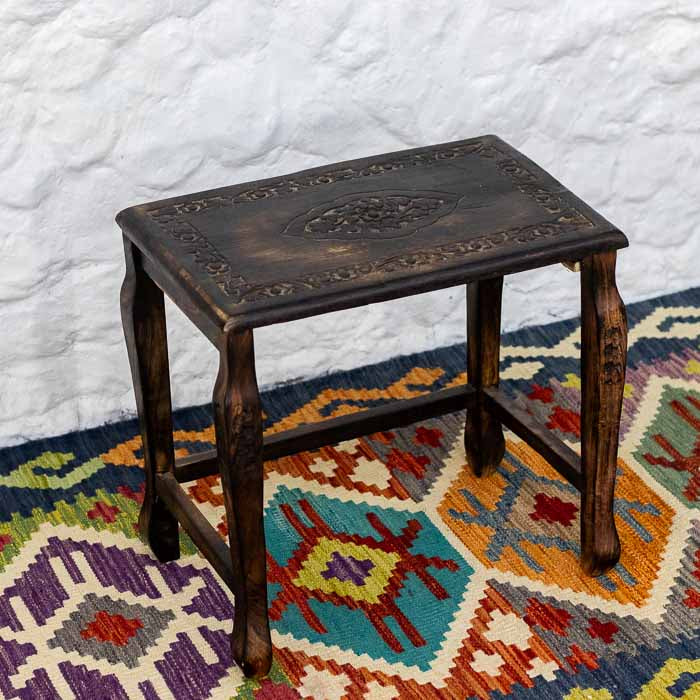 Mesa de apoio em madeira entalhada à mão com brasão central floral e borda ornamentada.
