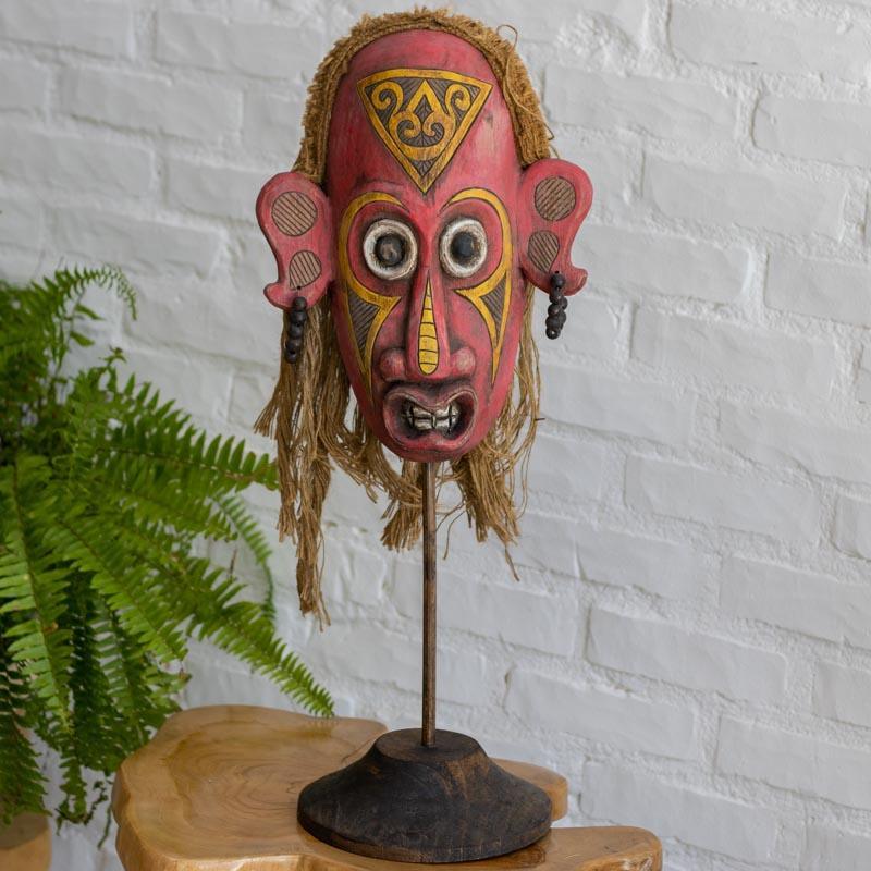Máscara decorativa de 40cm com adornos em fibras naturais e contas de madeira, integrando arte tribal e texturas orgânicas. 