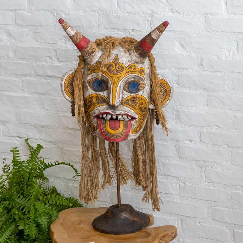Máscara decorativa de 40cm com adornos em fibras naturais e brincos de contas, integrando arte tribal e texturas orgânicas.