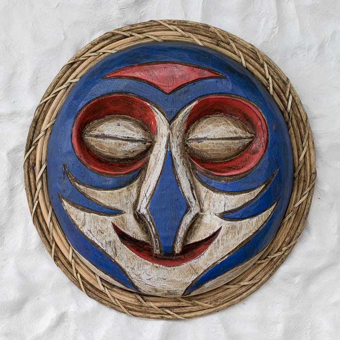 Máscara Bijak artesanal de Bornéu feita à mão em madeira com moldura em fibra natural, pintura azul e vermelha e acabamento rústico tradicional.