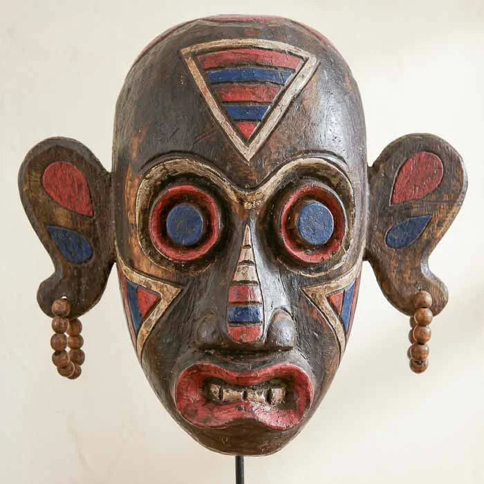 Escultura de máscara em madeira com 40cm de altura, apresentando entalhes manuais e pintura de volutas tradicionais dos povos de Bornéu. 