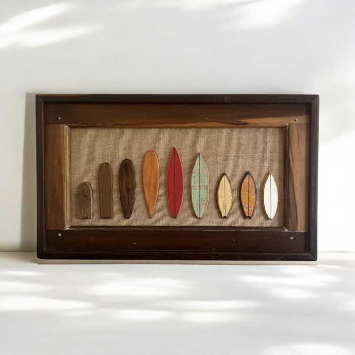 Quadro decorativo artesanal Surf Evolution criado por Márcio Delfino, com miniaturas de pranchas esculpidas em madeira sobre juta.