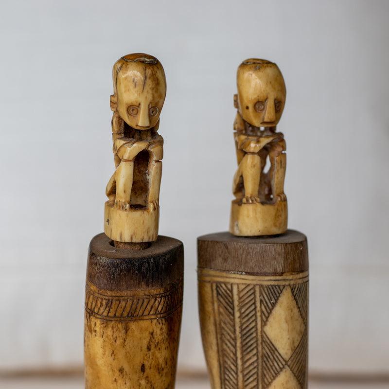 Obra decorativa em osso entalhado com figura de homem em cócoras.