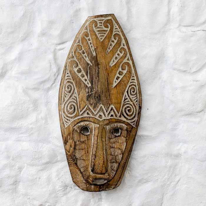 Máscara tribal de Timor-Leste em madeira rústica com entalhes manuais em relevo claro.