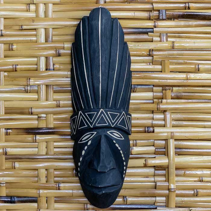 Máscara indígena de parede feita à mão em madeira escura com pintura branca.