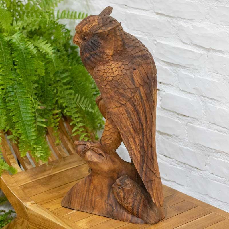 Escultura naturalista de coruja sobre tronco de madeira com veios orgânicos aparentes. 