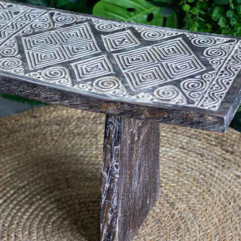 Detalhe dos entalhes geométricos e espirais em baixo relevo no assento de madeira, destacando a cultura primitiva da Indonésia.