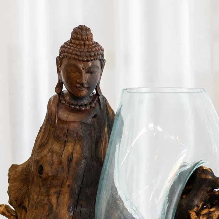 Detalhe da face serena de Buda em escultura de tronco rústico integrada a vaso de vidro transparente. 