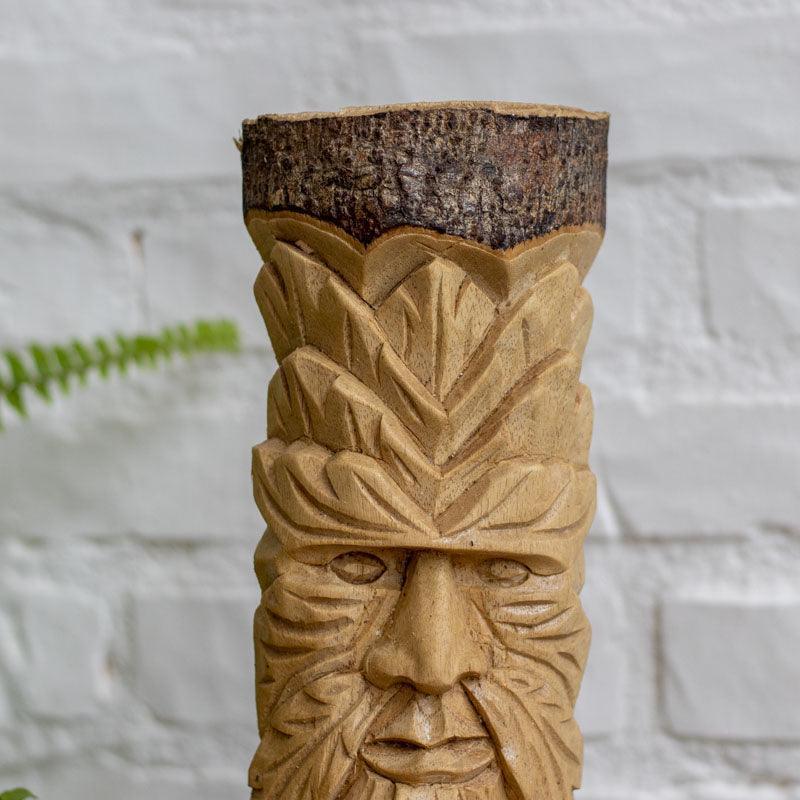 Objeto decorativo artesanal com rosto do homem verde esculpido em madeira bruta. 