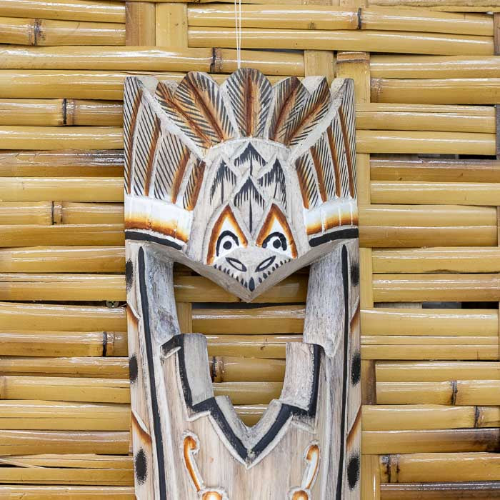 Peça artesanal de parede com faces tribais entalhadas em madeira.
