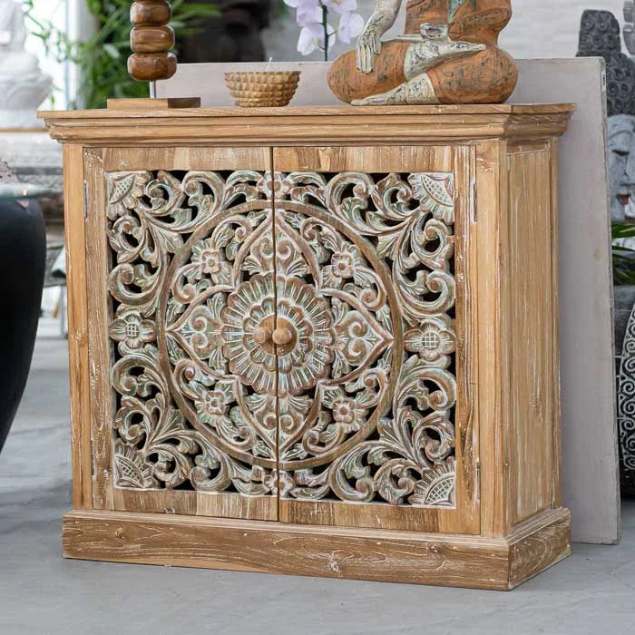 Estante artesanal em madeira com portas entalhadas em forma de mandala floral e acabamento em pátina branca e verde, feita à mão por artesãos de Bali.
